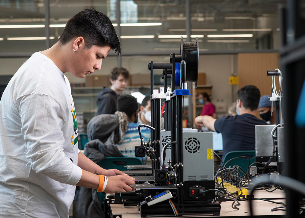 A student stands at a 3D printer, setting up a print.